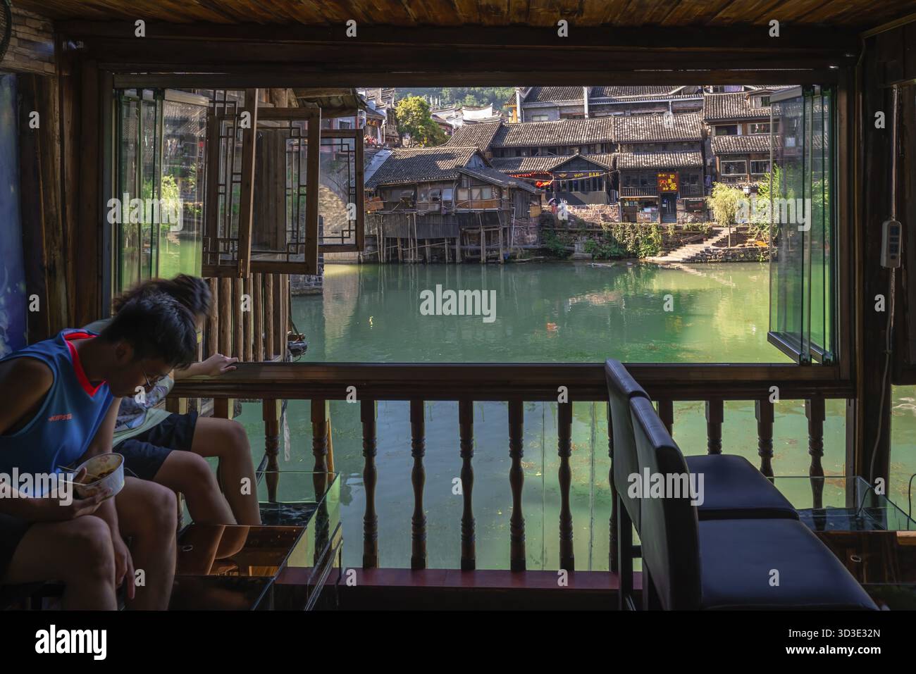 Feng Huang, Cina - agosto 2019: Uomo e donna cinesi che tengono i piedi in un serbatoio d'acqua pieno di pesci rufa garra in spa cinese pedicure cura della pelle t Foto Stock