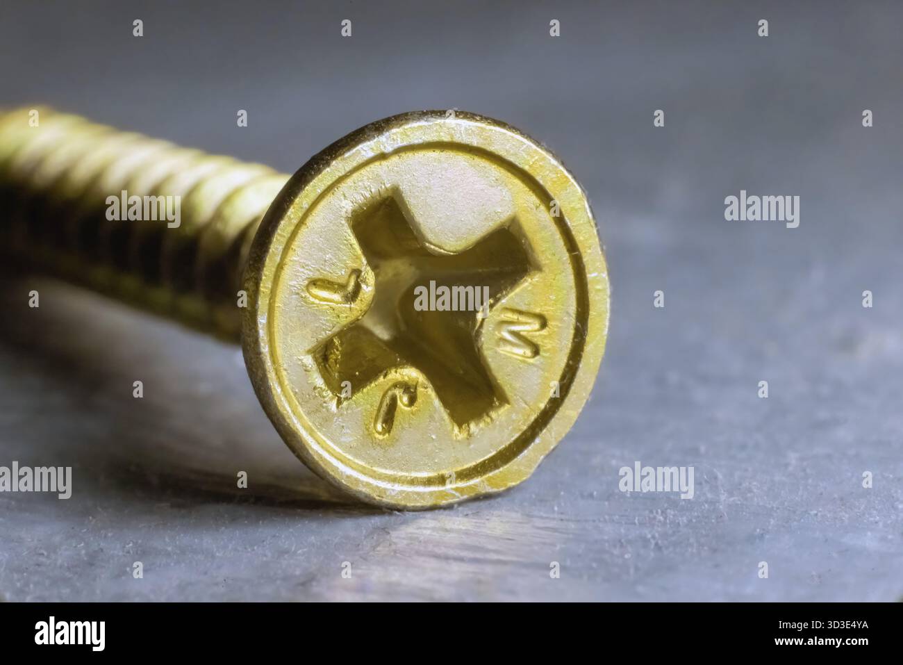Una testa a vite gialla a testa Phillips, parzialmente incorporata in una superficie, presenta i bordi seghettati e una sottile marcatura Foto Stock
