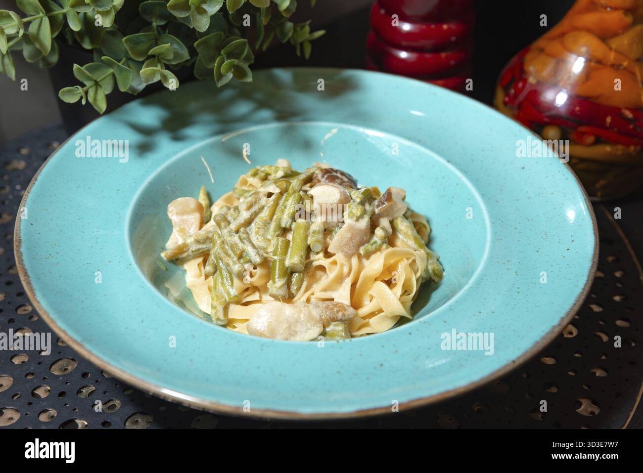 Cibo, deliziose tagliatelle cremose condite con asparagi verdi saltati e funghi serviti in un vivace piatto turchese Foto Stock