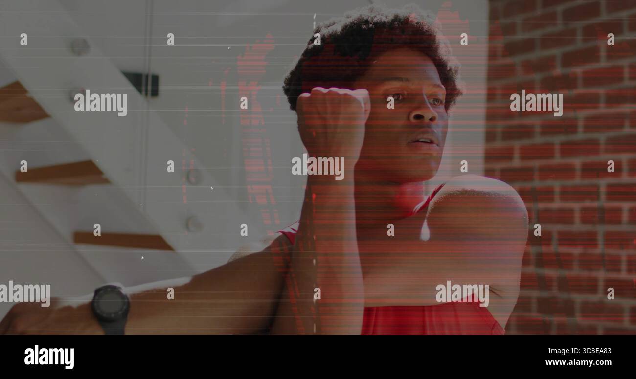 Uomo che indossa una camicia sportiva rossa e uno smartwatch che si allunga sul petto a casa, con parete in mattoni Foto Stock