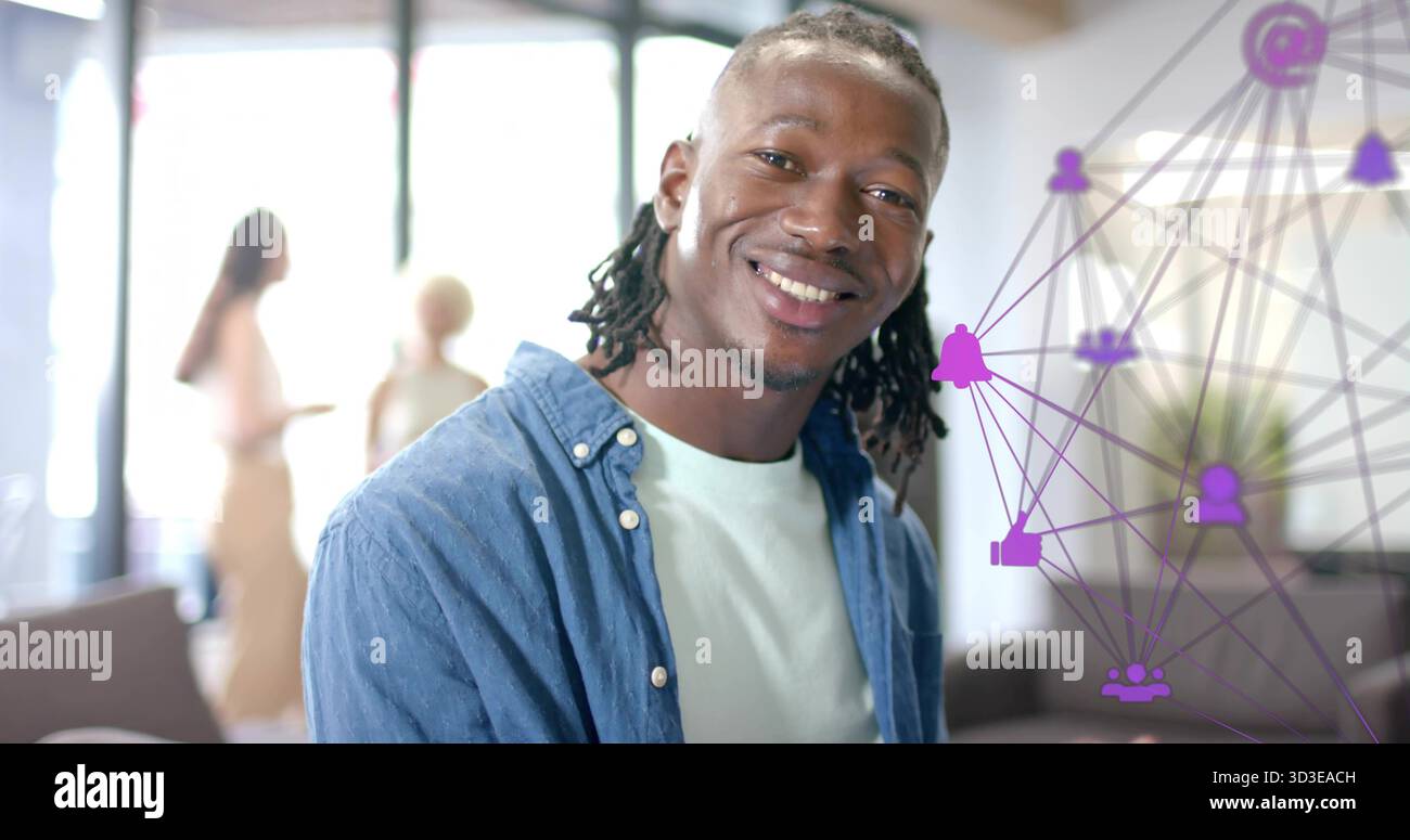 Uomo sorridente con trecce che indossano una camicia in denim nella lounge, team che parla vicino alle finestre, rivestimento viola Foto Stock