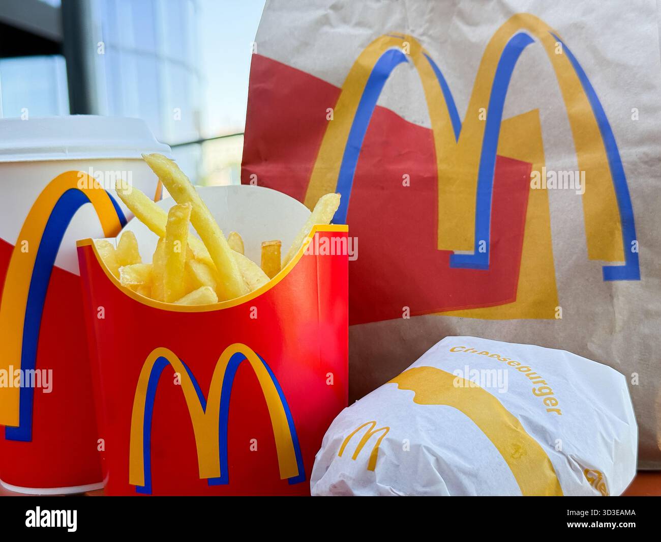 McDonald's ordina sul tavolo della terrazza all'aperto: Sacchetto di carta con marchio, patatine fritte fresche, hamburger e una bevanda da vicino Foto Stock