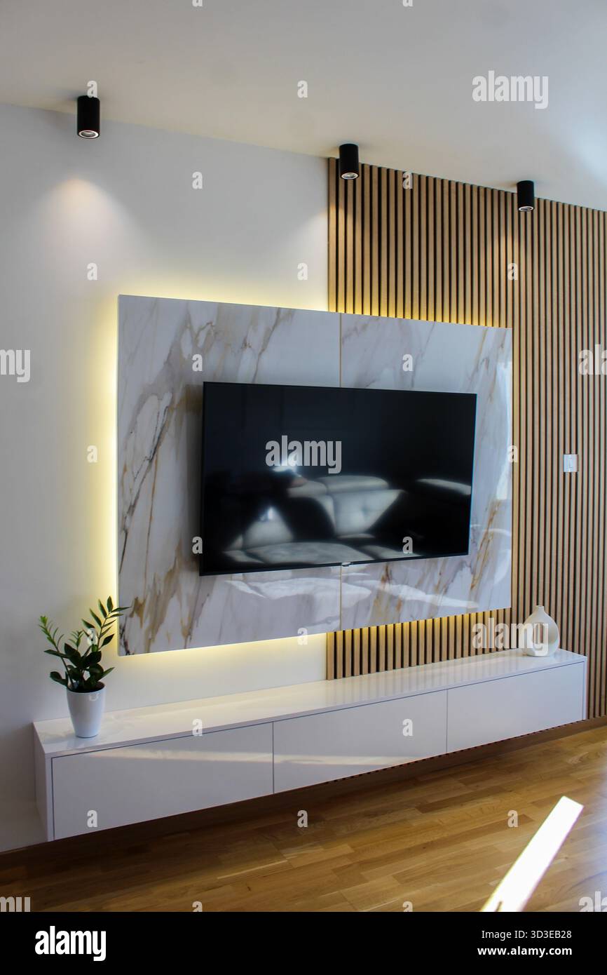Elegante parete TV con pannelli in marmo, listelli in legno e illuminazione a LED, che combina design moderno con materiali naturali. Foto Stock