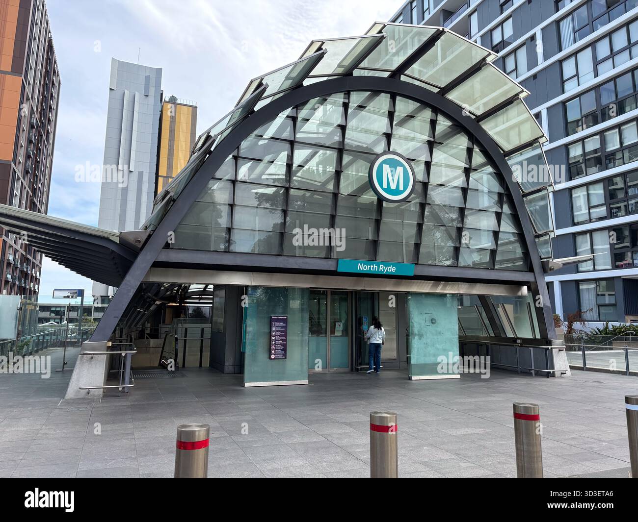 North Ryde Metro Station, Sydney, Australia. Moderno ingresso in vetro ad arco e acciaio con logo "M". Un fulcro chiave dei trasporti pubblici in una contemporaneità Foto Stock