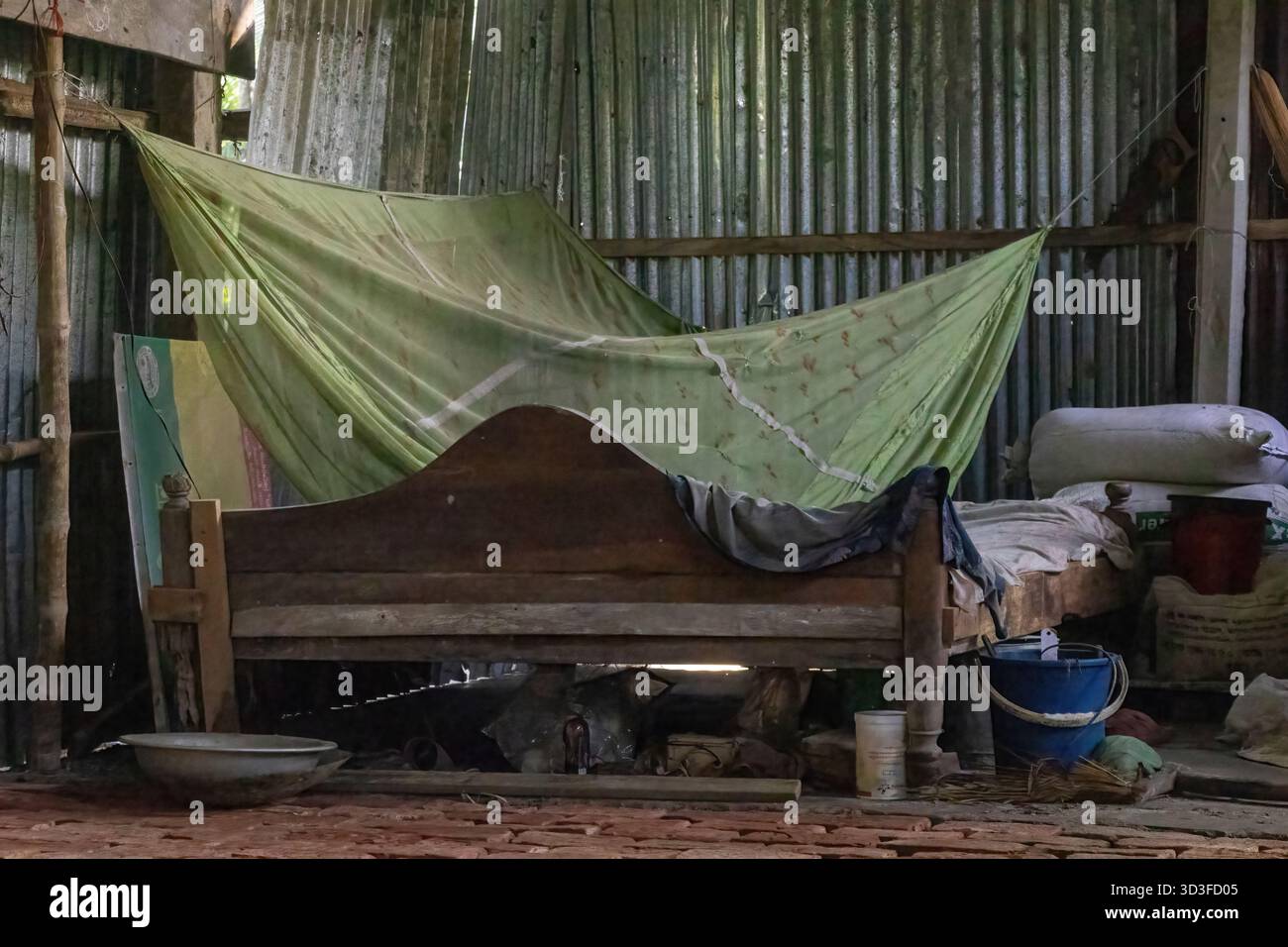 Vista interna di una casa rurale molto disordinata e povera in Bangladesh, caratterizzata da un semplice e vecchio letto in legno con zanzariera protettiva (o Foto Stock