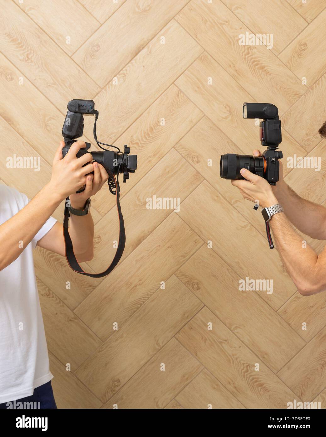 Uno scatto ravvicinato di due fotografi con fotocamere digitali professionali e unità flash, pronti a catturare un attimo. Sono in piedi contro un elegante legno Foto Stock