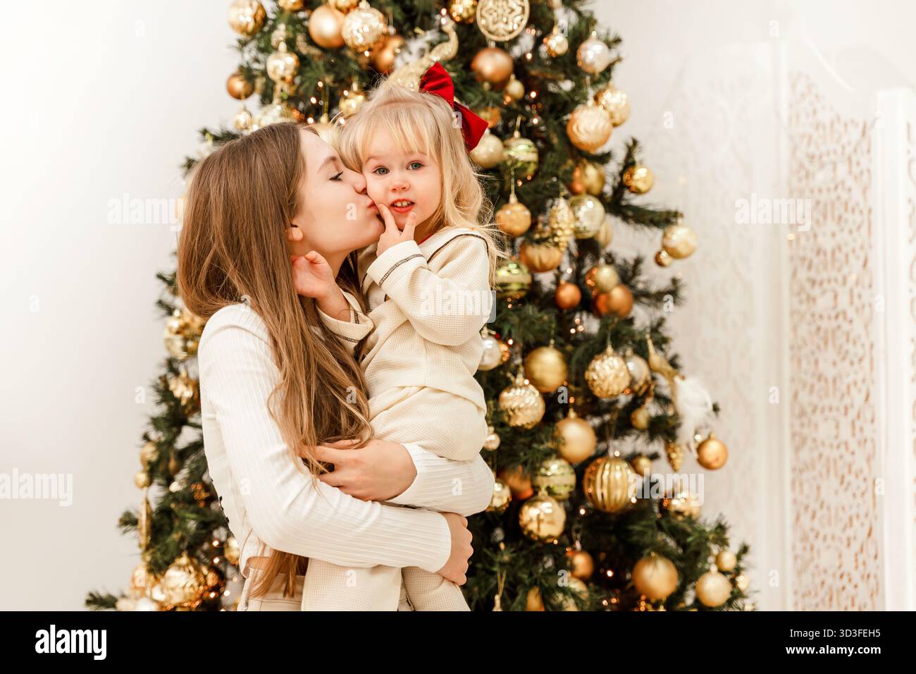 Due sorelle, una adolescente e una bambina di 3 anni, si abbracciano accanto a un albero di Natale decorato. Decorazioni per la casa per il nuovo anno. Tradizioni di famiglia Foto Stock