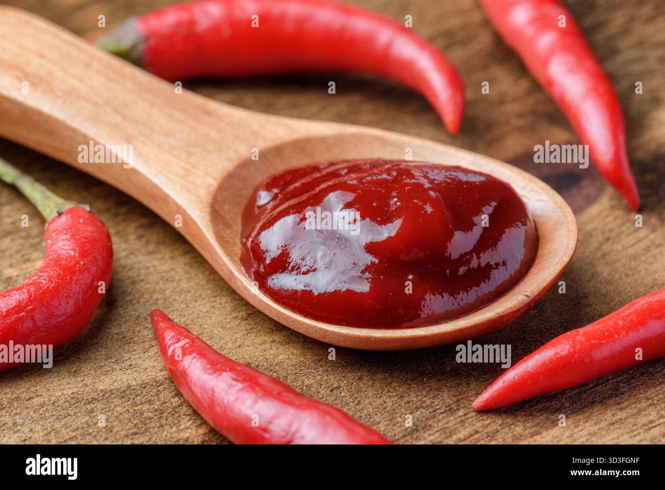 Cucchiaio di legno di pasta di peperoncino piccante tra peperoncini freschi Foto Stock
