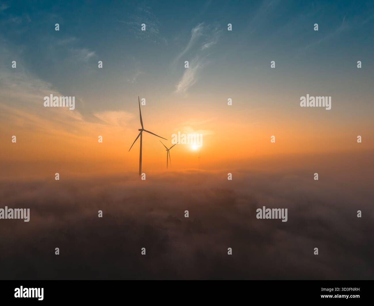 Turbine eoliche che si innalzano al di sopra di un paesaggio nebbioso all'alba con una luce calda Foto Stock