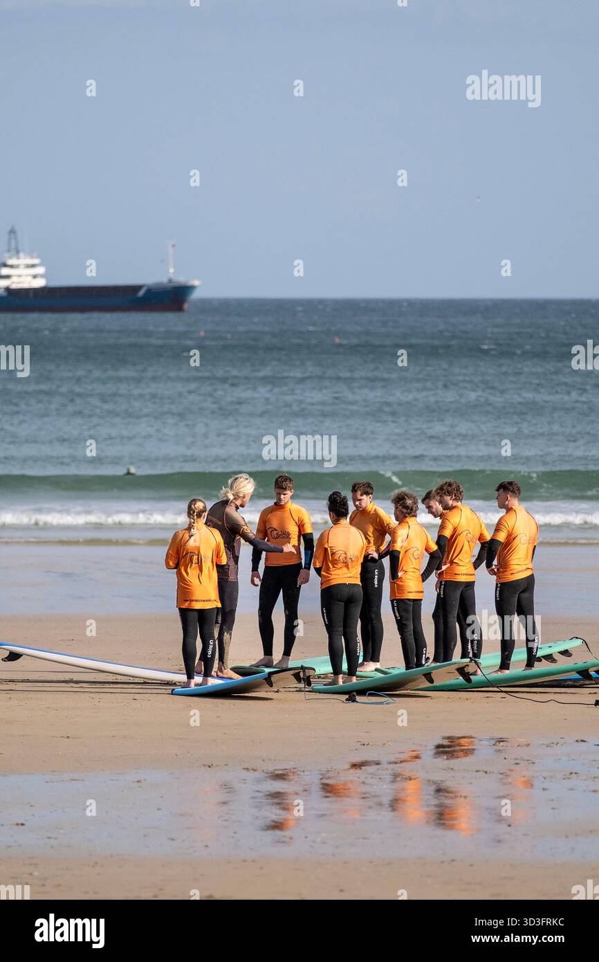Un gruppo di vacanzieri in una lezione di surf con un istruttore della Cornish Wave Surf School presso Towan Beach a Newquay, in Cornovaglia, in Inghilterra Foto Stock