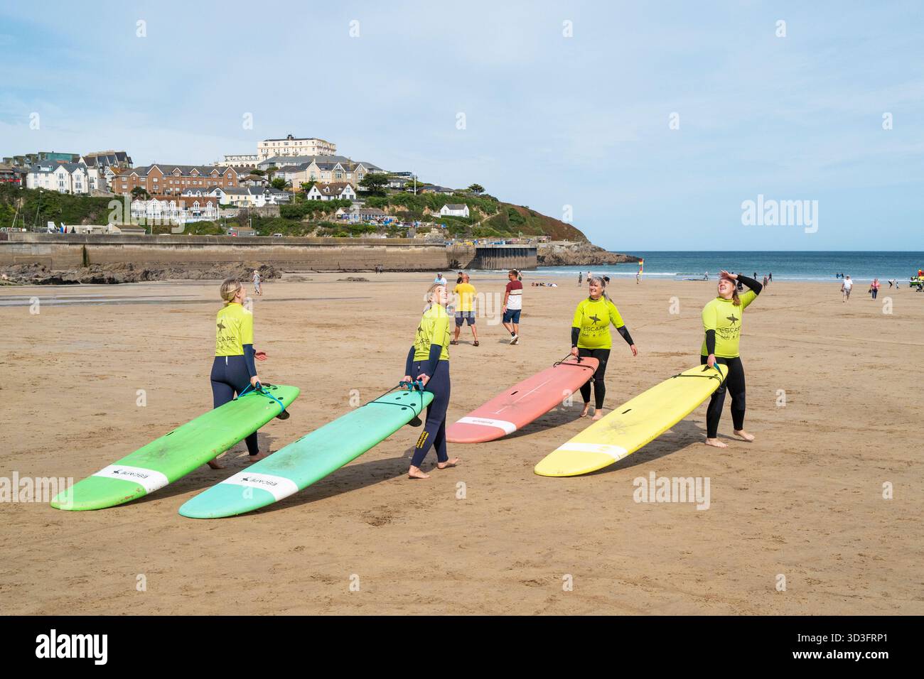 Un gruppo di ragazze principianti del surf che trascinano le loro tavole da surf al mare a Towan Beach in preparazione per una lezione di surf con Escape Surf School in N Foto Stock