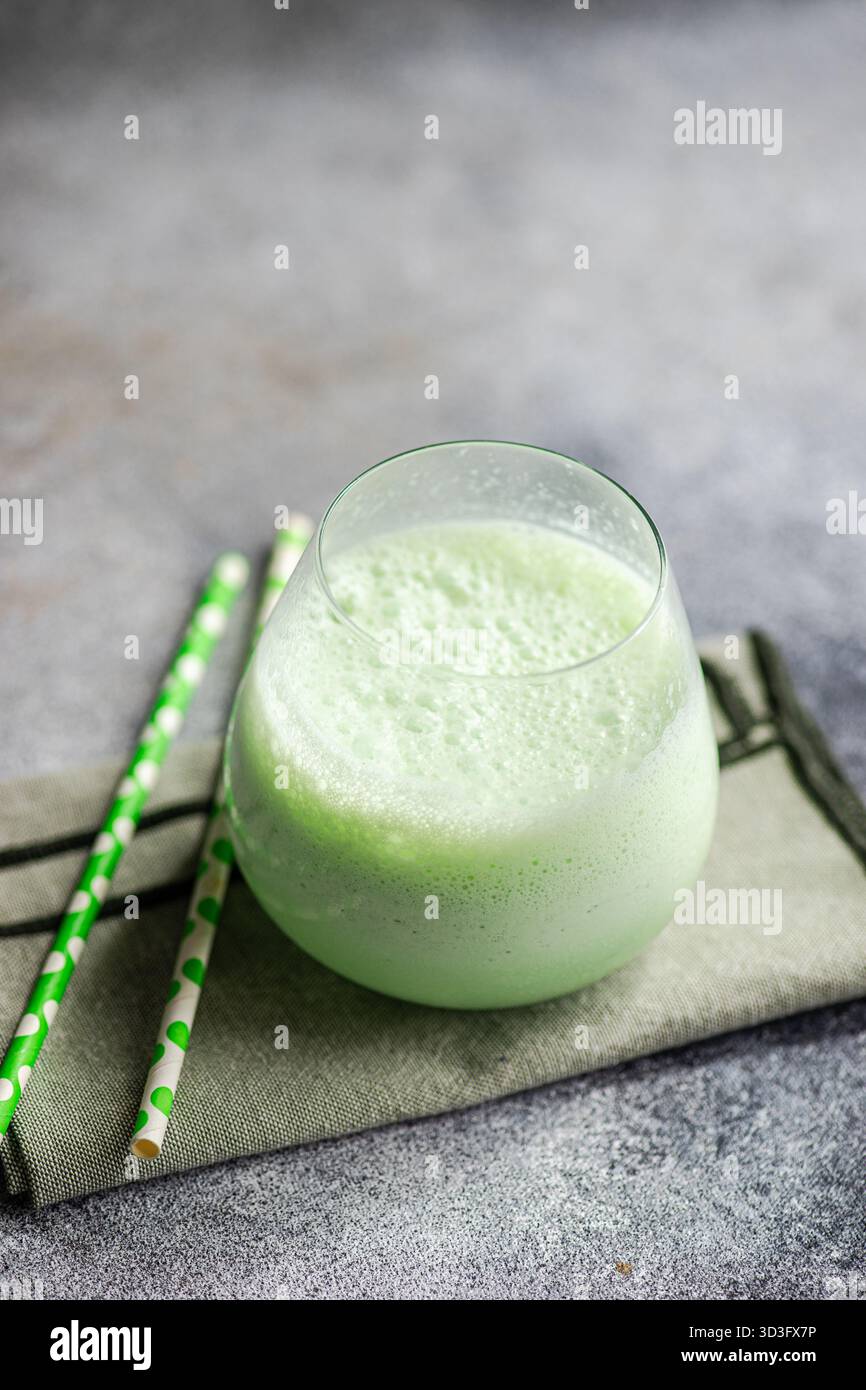 Un rinfrescante latte matcha in un bicchiere, ricoperto di schiuma di latte. La vivace bevanda verde è completata da due cannucce di carta verde, fotografate su una Foto Stock