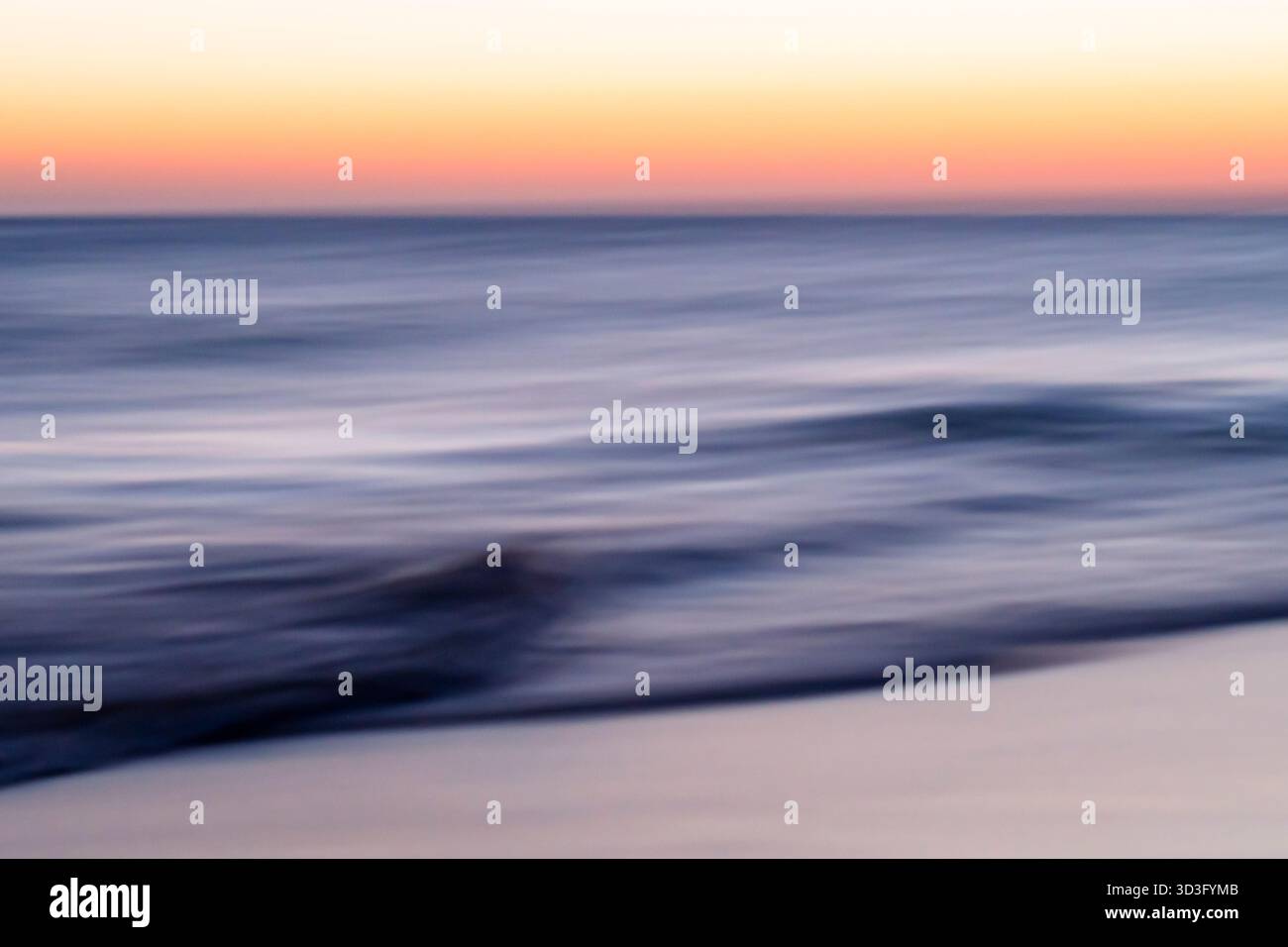 Una splendida vista del mare all'ora d'oro, con onde dolci che riflettono le calde sfumature del tramonto. Il gradiente morbido dei colori cattura un pe sereno Foto Stock