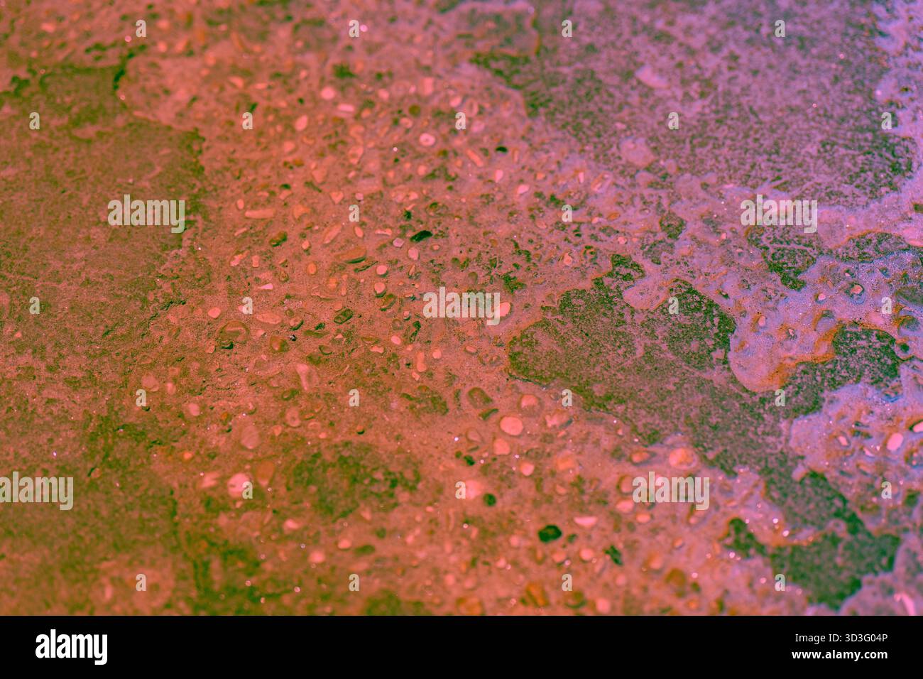 Primo piano di una superficie rocciosa ruvida con sfumature rossastre e verdi, che mostra formazioni naturali e ciottoli incorporati. Ideale per sfondi o design Foto Stock