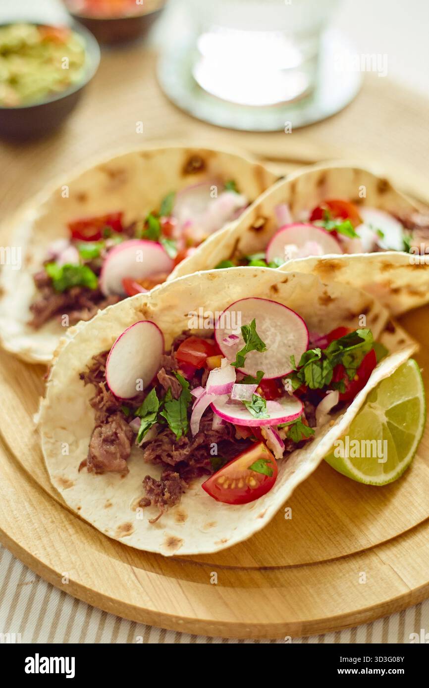 Tre deliziosi tacos ripieni di carne tenera, ravanelli, coriandolo e cipolle, guarniti con spicchi di lime. Una rappresentazione perfetta dell'autentico messicano Foto Stock