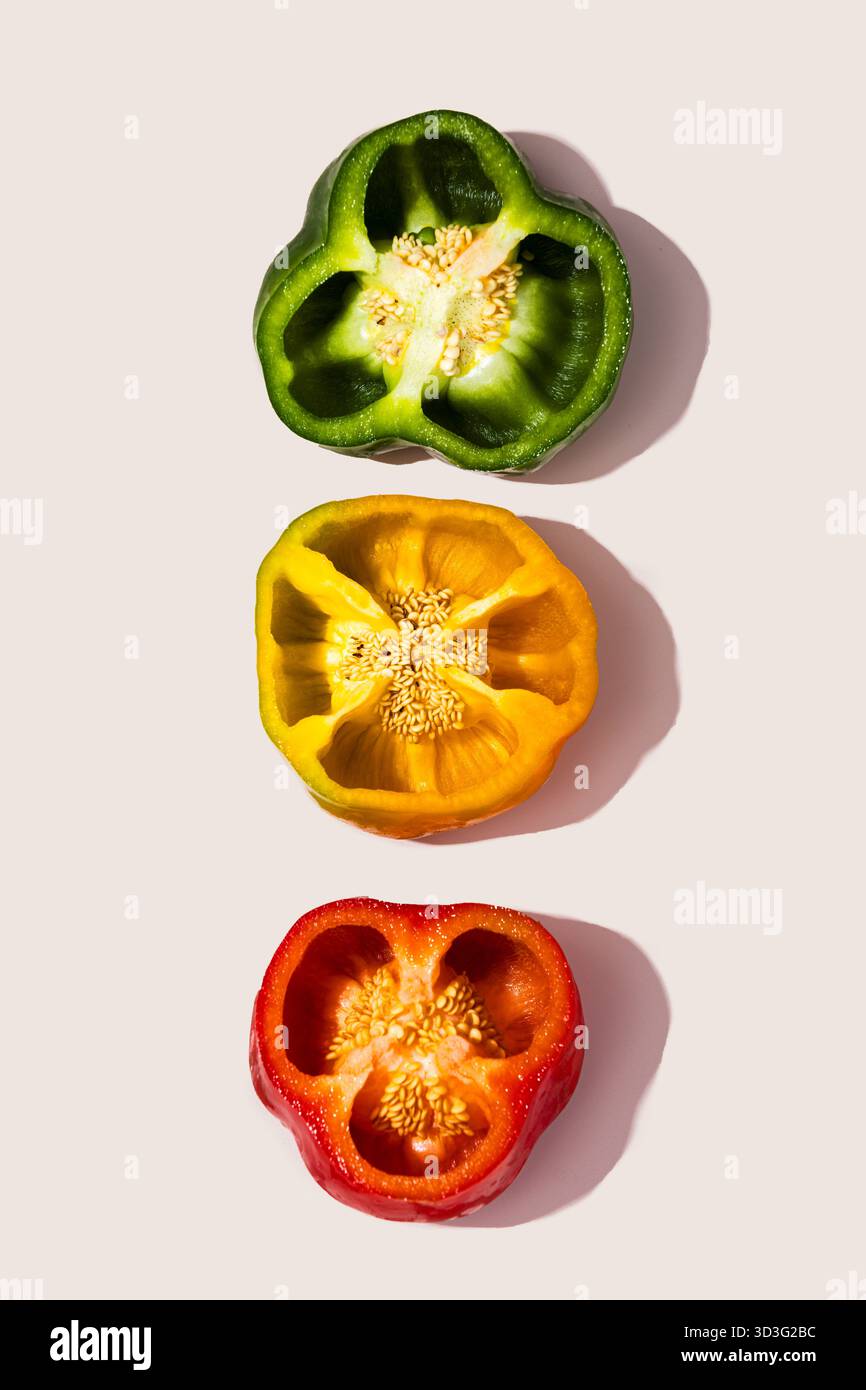 Un'immagine sorprendente che mostra tre peperoni tagliati in vivaci tonalità verde, giallo e rosso, disposti in modo ordinato su uno sfondo liscio e neutro. Perfetto f Foto Stock