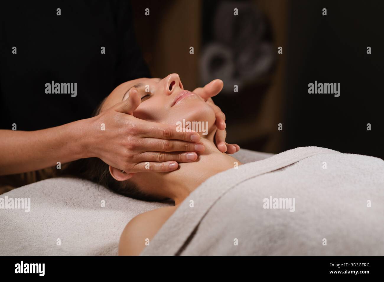 Una donna gode di un rilassante massaggio facciale in una spa benessere. Un terapista utilizza tecniche delicate ed efficaci per alleviare la tensione e promuovere il rilassamento Foto Stock