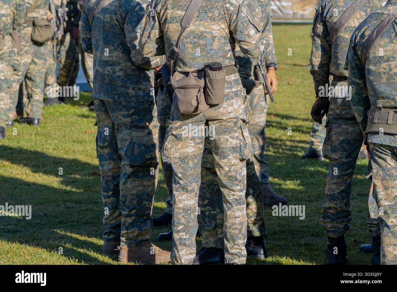 Diversi soldati in uniforme mimetica sono in piedi in un gruppo su un campo erboso. Foto Stock