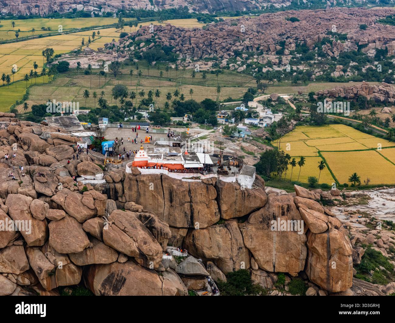 Vista aerea delle vivaci sfumature del tempio in cima all'aspra collina Matanga che contrasta con le risaie verdi, Hampi, Karnataka, India. Foto Stock