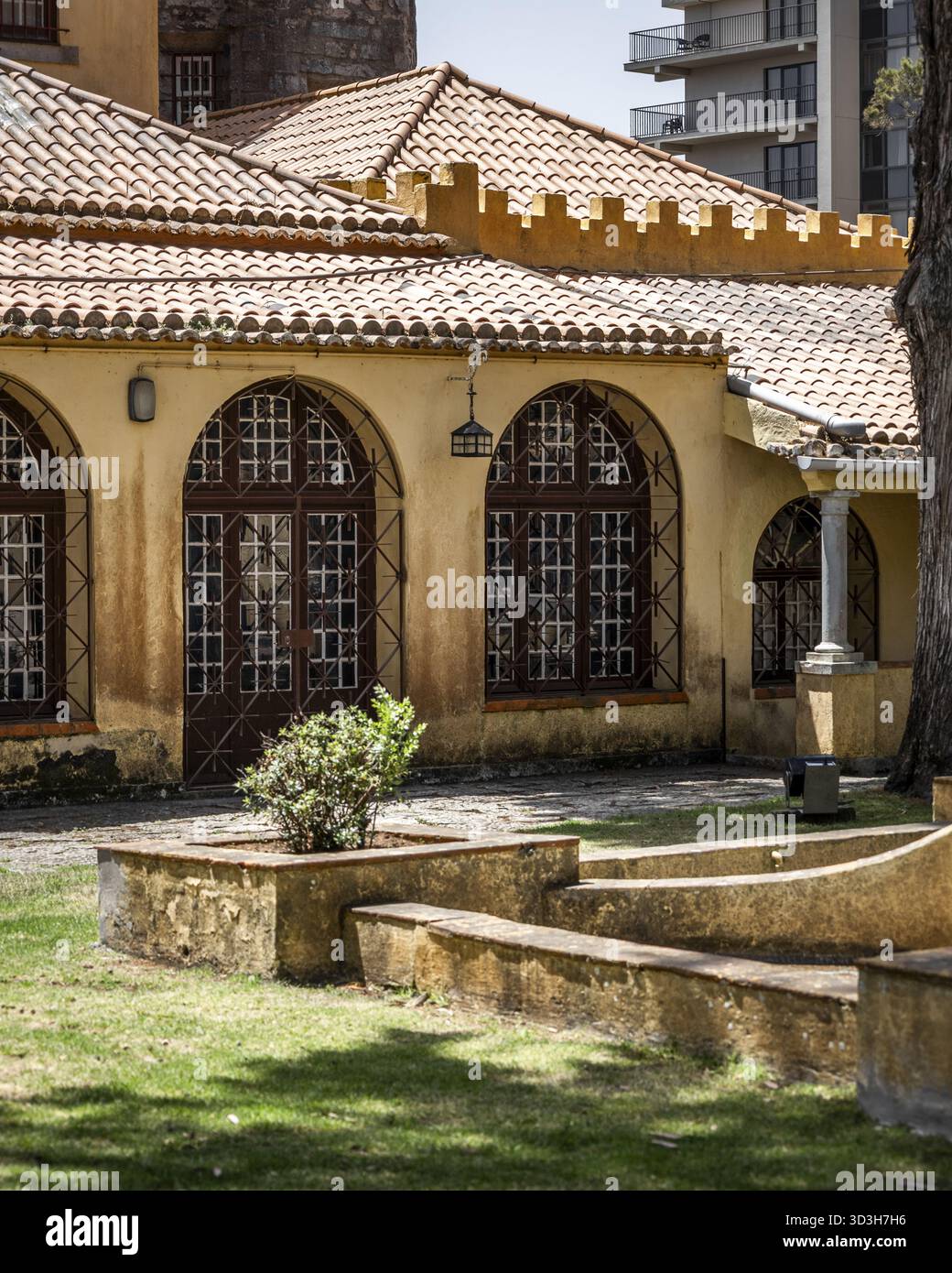 Vista della facciata gialla di un edificio con finestre ad arco con cornici di legno scuro e un tetto piastrellato, giustapposto all'architettura moderna, Cascais, L. Foto Stock