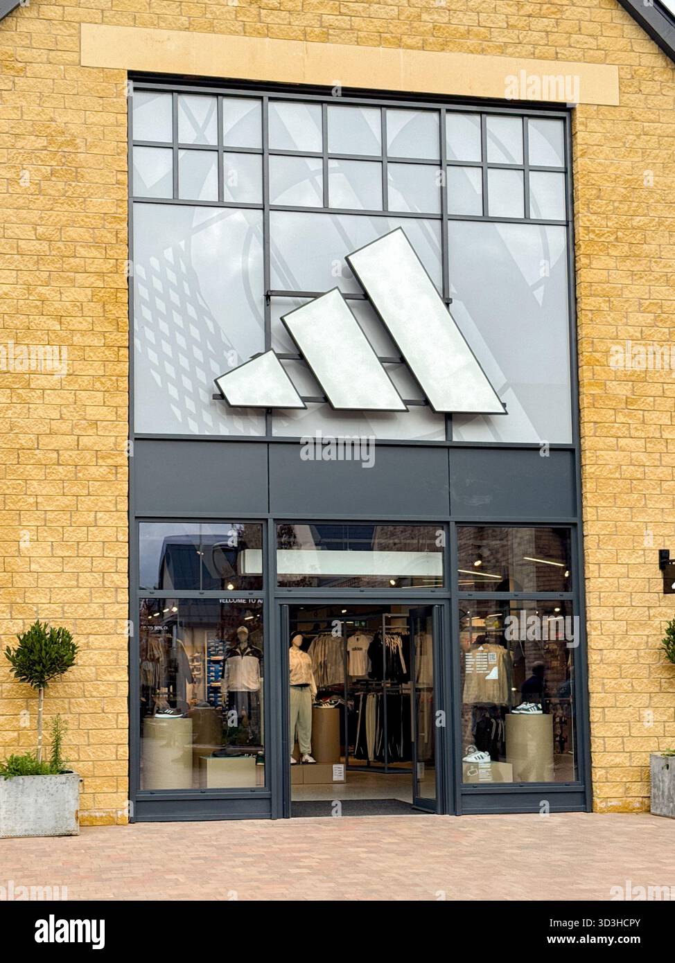 Tewkesbury, Gloucestershire, Inghilterra, Regno Unito - 10 ottobre 2025: Vista frontale dell'ingresso al negozio di abbigliamento sportivo Adidas nell'outlet Cotswolds Designer - Immagine stock catturata con smartphone