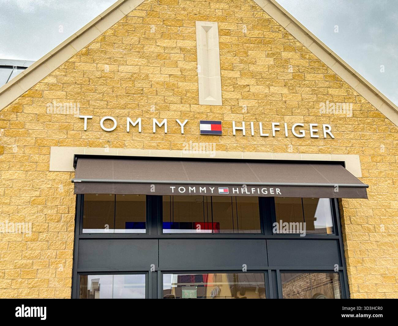 Tewkesbury, Gloucestershire, Inghilterra, Regno Unito - 10 ottobre 2025: Ingresso al negozio di stilisti Tommy Hilfiger nel Cotswolds Designer Outlet - Immagine stock catturata con smartphone