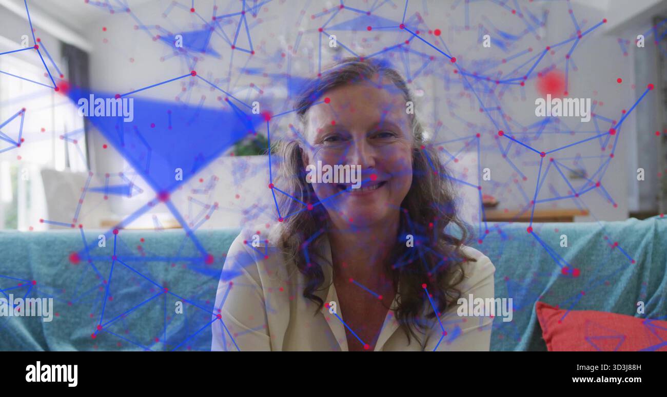 Donna matura seduta che indossa una camicetta leggera sul divano nel soggiorno, con laptop e sovrapposizione di rete Foto Stock