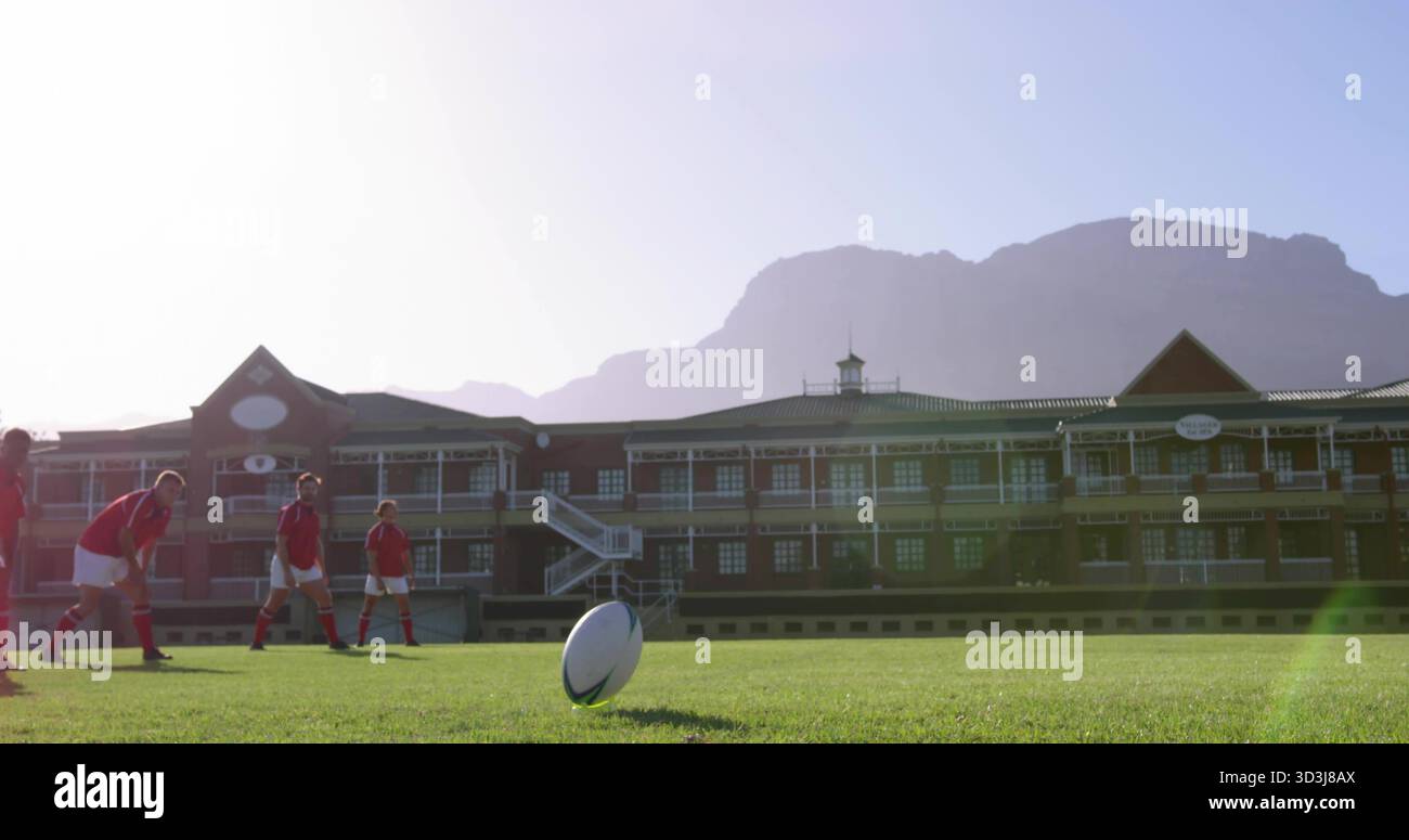 Posizionamento di cinque giocatori di rugby che indossano maglie rosse per preparare il calcio sul campo scolastico, con palla sul tee Foto Stock