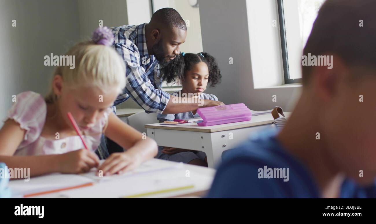 Insegnante di sesso maschile pendente che guida la pupilla seduto alla scrivania dell'aula, con astuccio per il libro degli esercizi Foto Stock