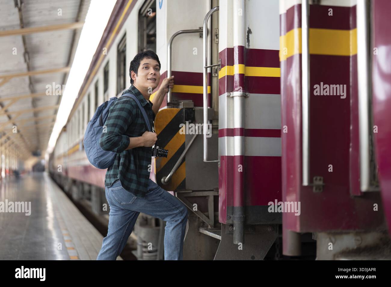 Eccitato per la sua prossima avventura, un giovane uomo si prepara a salire a bordo di un treno, mettendo in risalto l'emozione del viaggio e il viaggio in avanti con la sua macchina fotografica al seguito Foto Stock