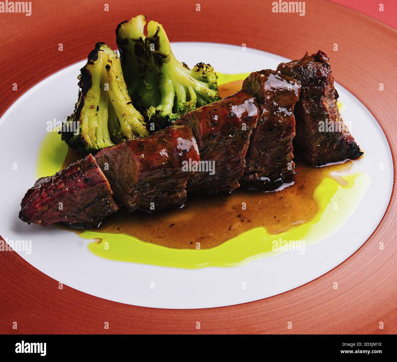 Cibo, maiale arrosto con salsa e broccoli su piatto rosso Foto Stock