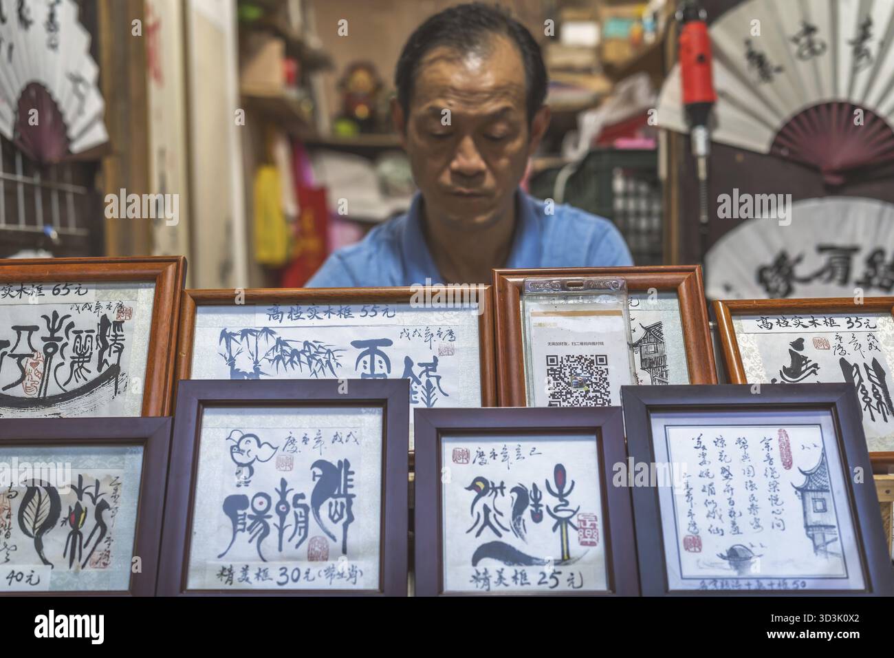 Chongqing, Cina - agosto 2019: Uomo che vende opere d'arte incorniciate nel negozio di caligrafia nella città antica di ci Qi Kou Foto Stock