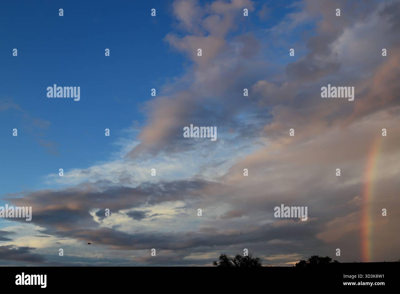 Arcobaleno serale parziale accanto alle nuvole di tempesta sopra Amsterdam, Paesi Bassi, con l'apertura del cielo blu e il cumulo a strati che si estende lungo l'orizzonte della città. Foto Stock