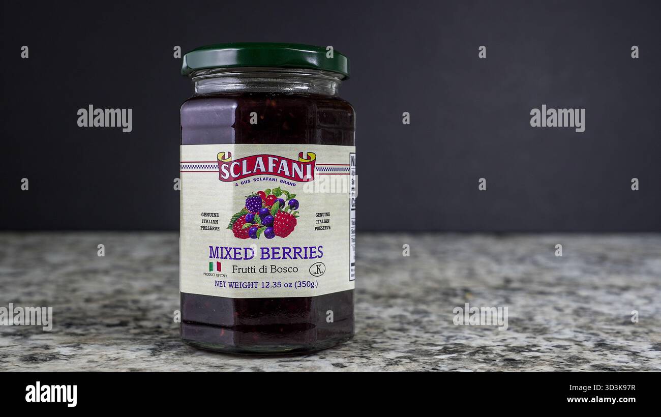 NORWALK, CT, USA - 30 OTTOBRE 2025: Un barattolo di marmellata mista di frutti di bosco viene posizionato su un piano di lavoro scuro. L'etichetta mostra frutta colorata che mostra il pr Foto Stock