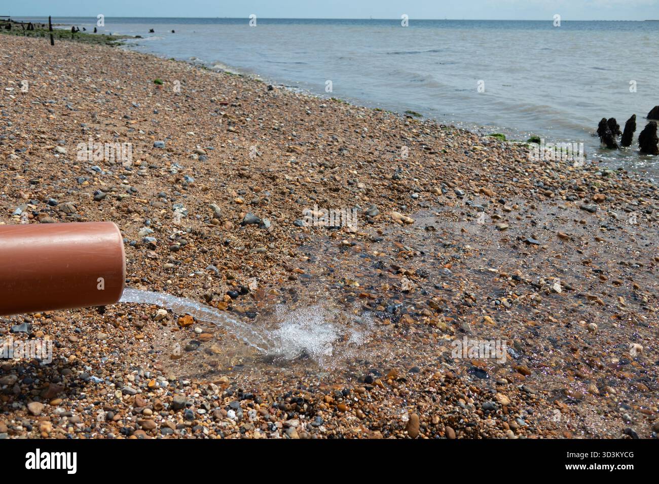 L'acqua che scorre fuori dal tubo sulla spiaggia di West Mersea nell'Essex, Inghilterra Foto Stock