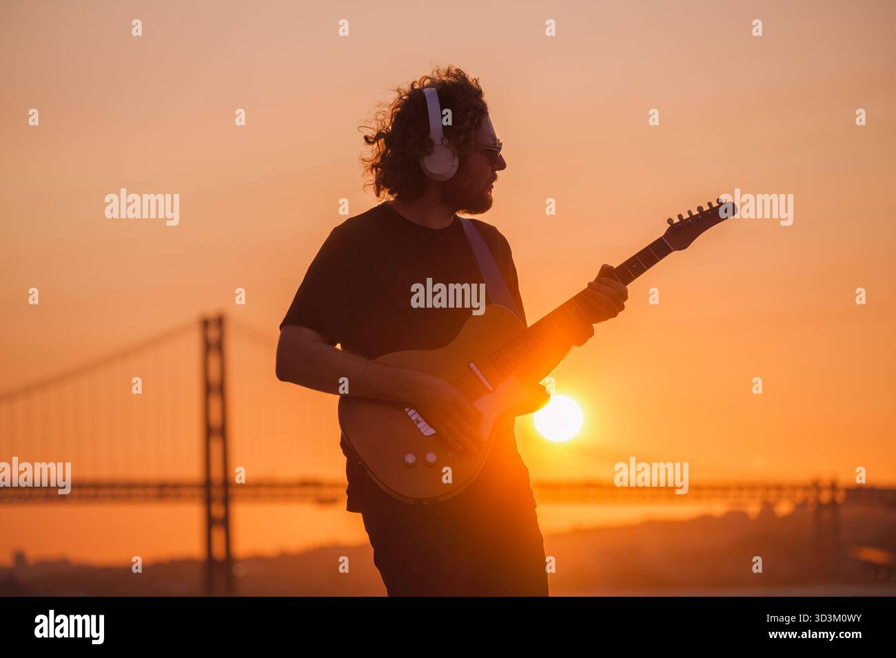 Musicista hipster di strada in nero che suona la chitarra elettrica in strada all'aperto al tramonto con luce parassita e perdita di luce Foto Stock