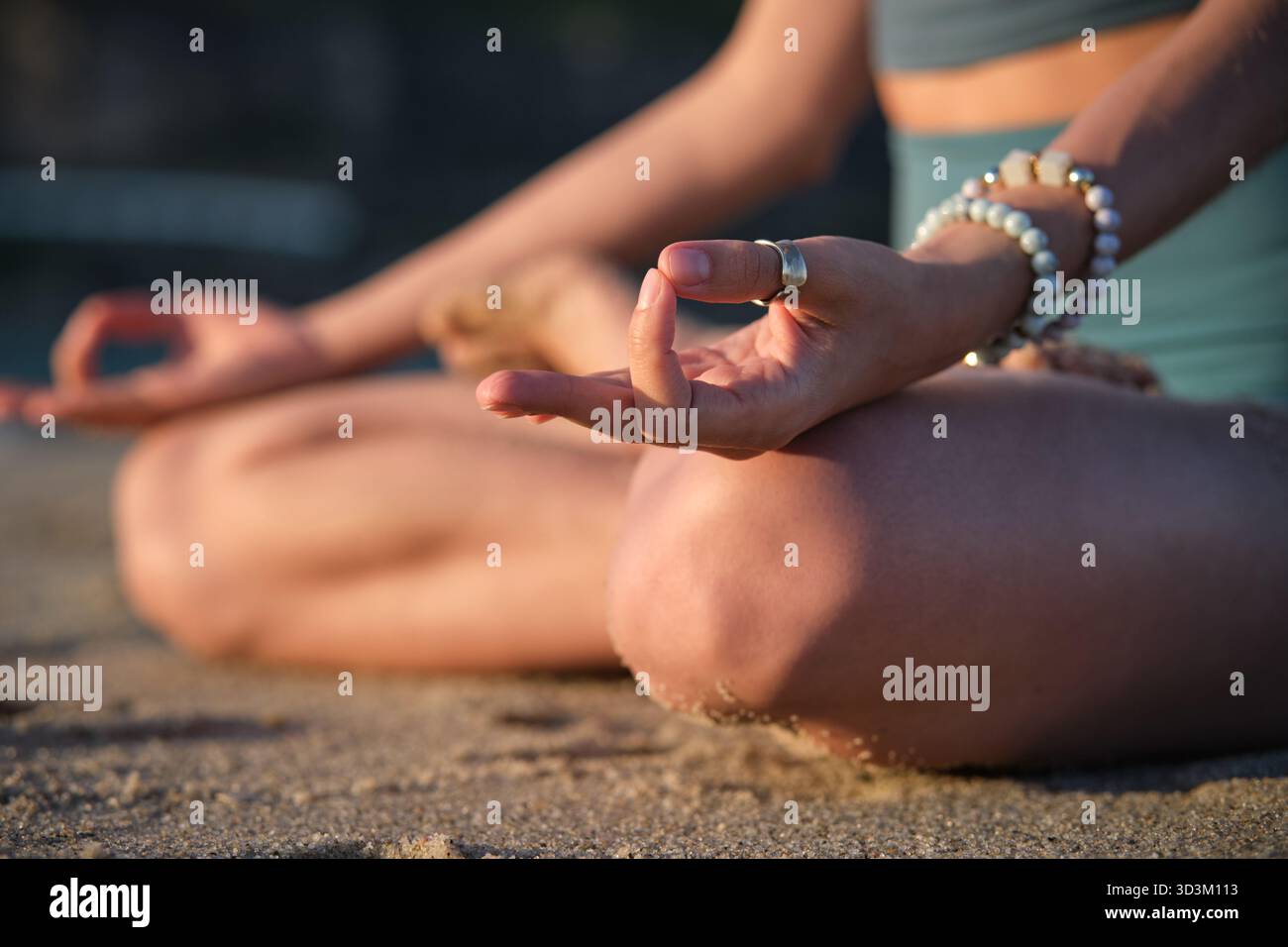 La donna medita a Padmasana sulla spiaggia, usando il gesto della mano Chin mudra in un ambiente tranquillo durante il tramonto. Foto Stock