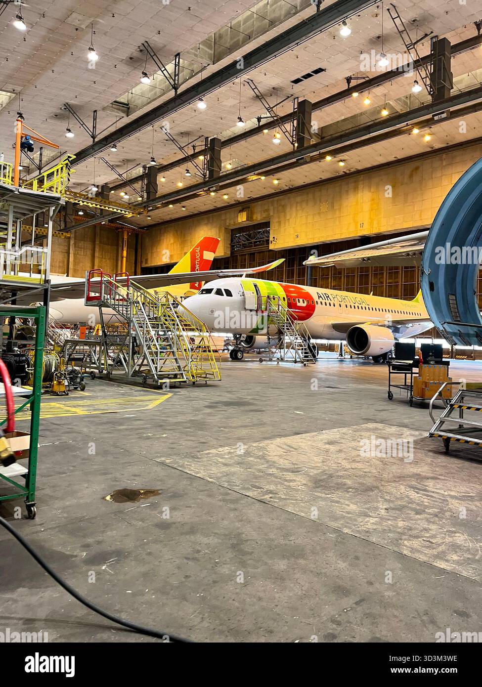 Gli aeromobili TAP Air Portugal sono in manutenzione all'interno di un grande hangar della compagnia aerea con ponteggi e attrezzature visibili. - Immagine stock catturata con smartphone