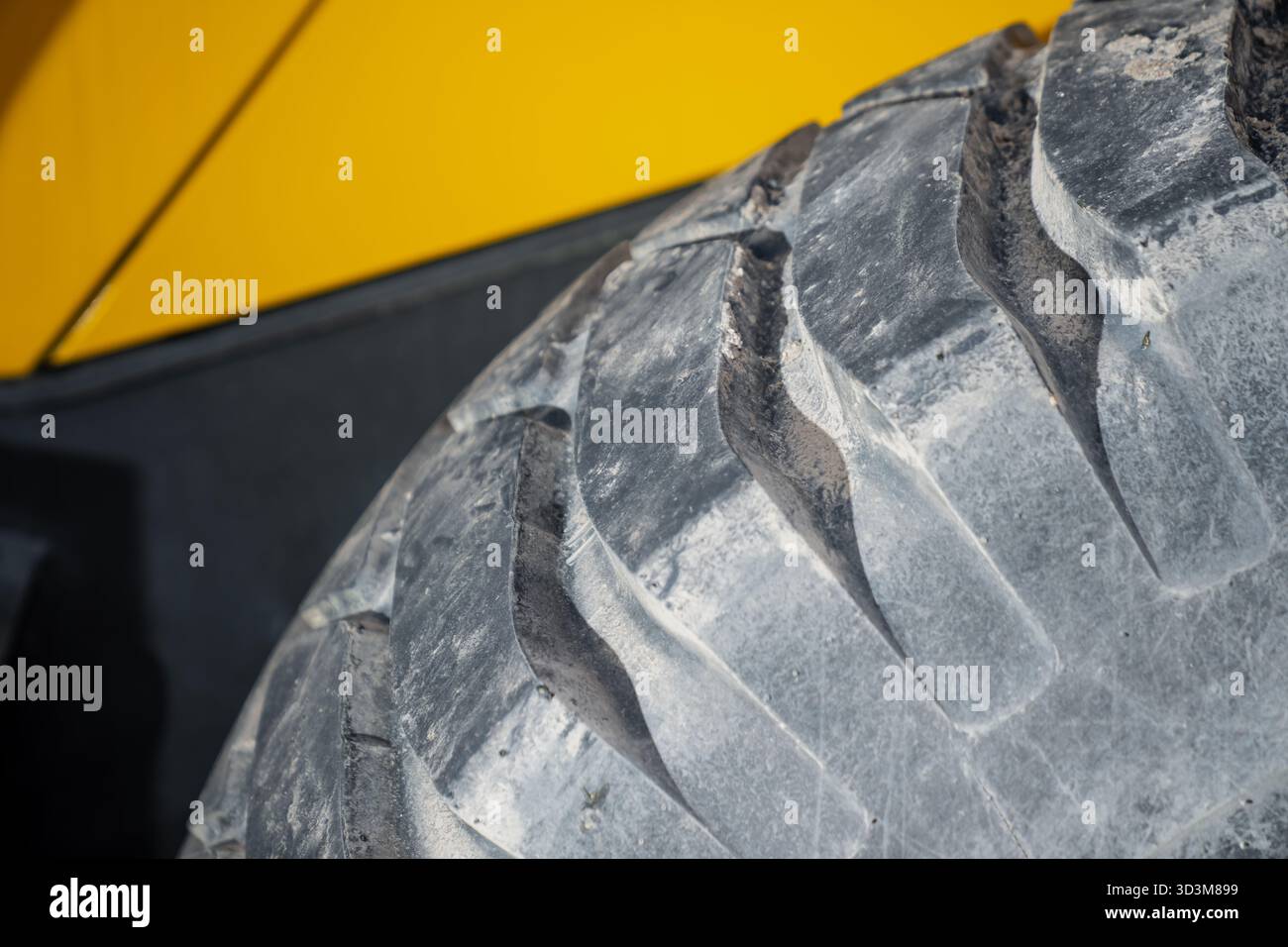 Chiudere il battistrada degli pneumatici dei veicoli da costruzione pesanti con scanalature molto usurate e accumulo di polvere contro la carrozzeria gialla che mostra la str. Industriale Foto Stock