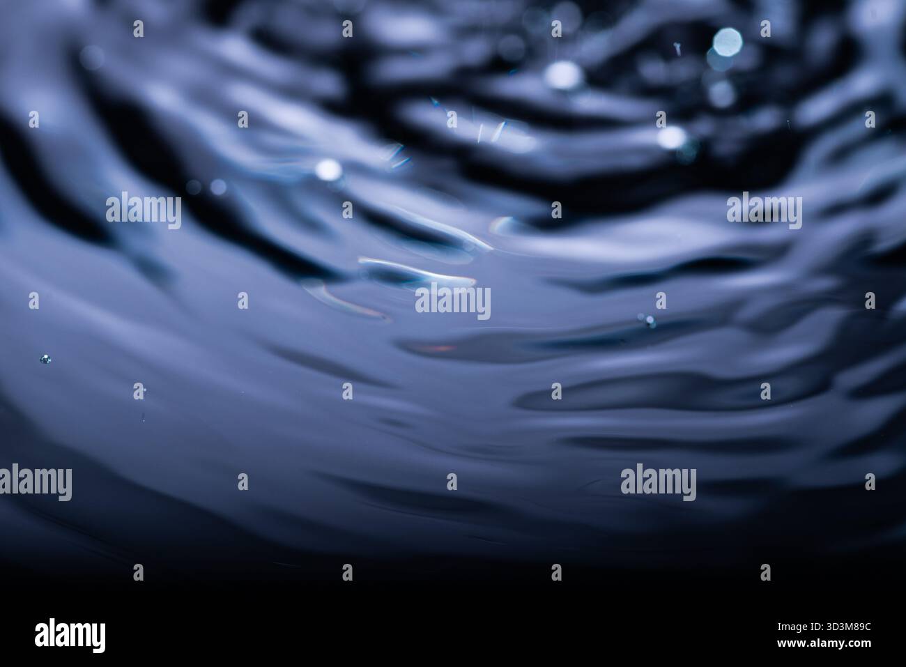 281.primo piano della superficie blu scuro dell'acqua che mostra increspature concentriche e riflessi di luce. Piccole goccioline e striature aggiungono una texture dinamica. Movimento fluido Foto Stock