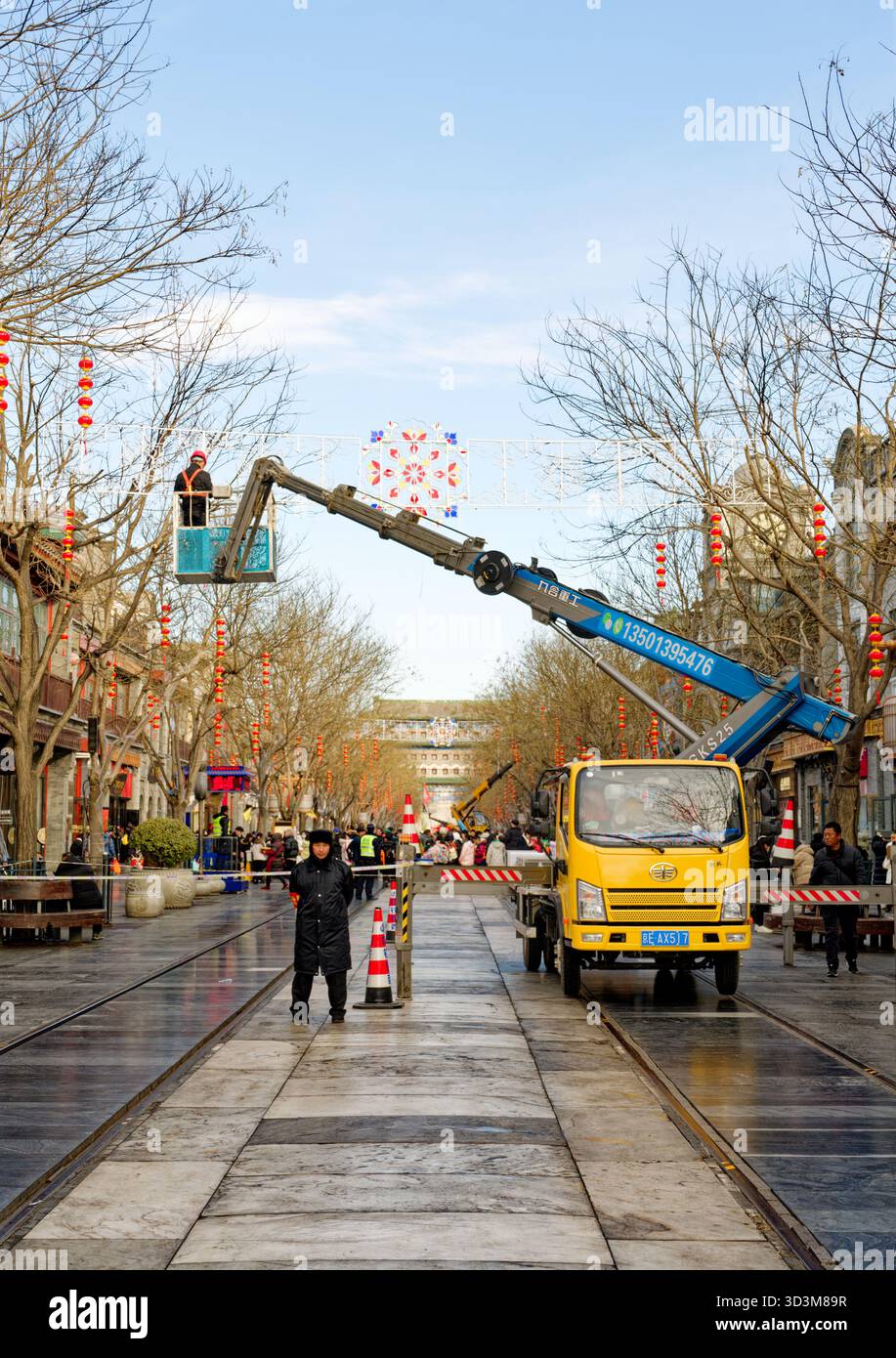 I lavoratori installano decorazioni natalizie per le strade utilizzando una gru lungo un viale fiancheggiato da lanterne a Pechino, preparandosi per il prossimo Capodanno cinese Foto Stock