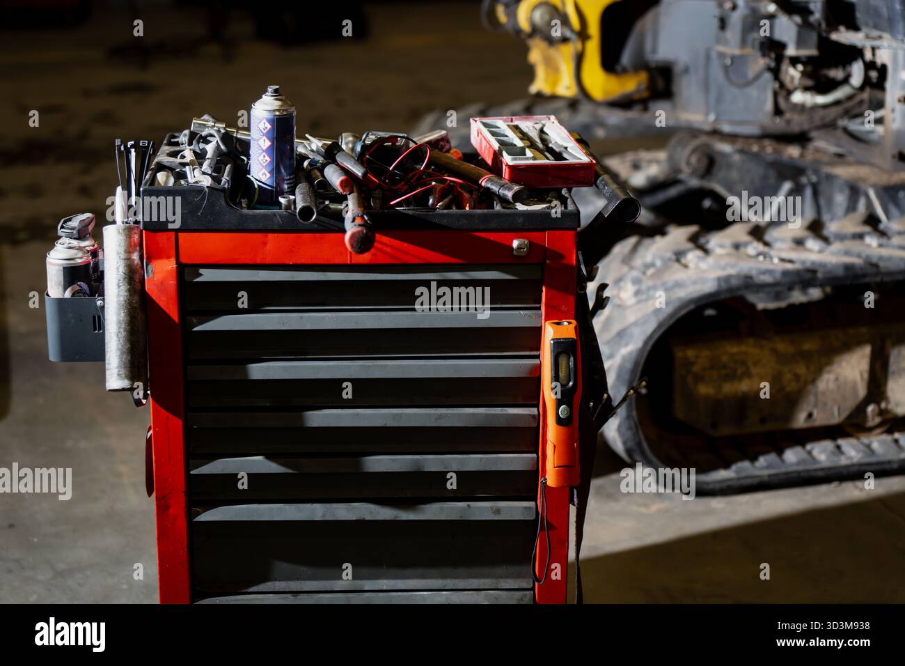 Postazione di lavoro per meccanici industriali con cassetta degli attrezzi rossa e attrezzature vicino a macchinari per l'edilizia pesante che mostrano utensili organizzati, materiali di riparazione ed ENG Foto Stock