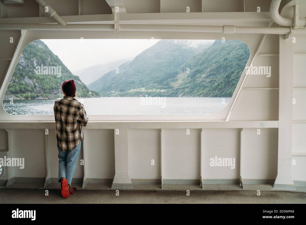 Donna che gode dei paesaggi dei fiordi sul traghetto norvegese con montagne verdi nebbiose sullo sfondo. La scena cattura l'essenza del viaggio rilassato, dell'esplorazione Foto Stock