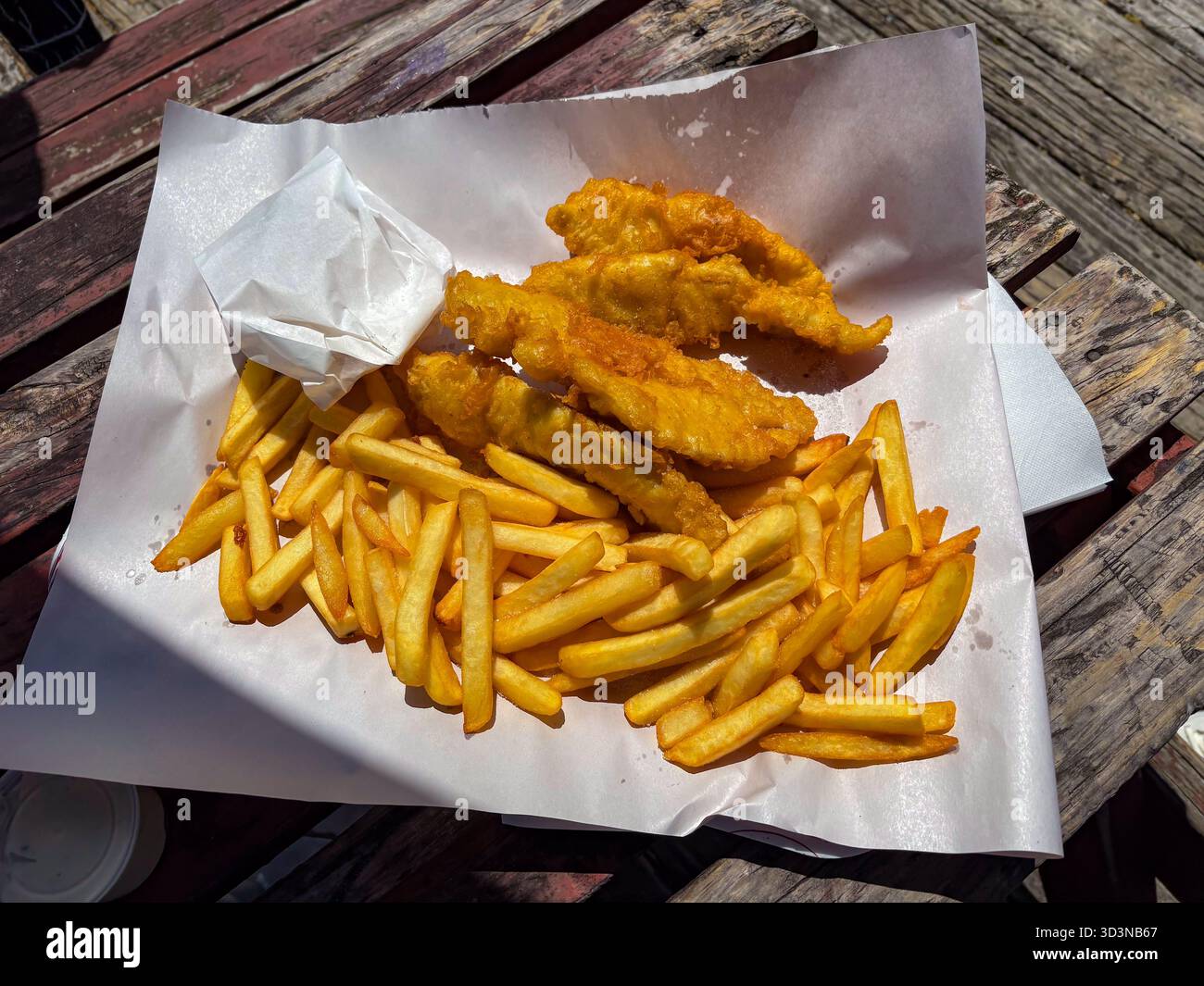 Fish and chips servito su carta dal Bobbys Fresh Fish Market, sul lungomare di Tauranga. Pesce pastella dorato e patatine fritte croccanti su una rustica linguetta di legno Foto Stock