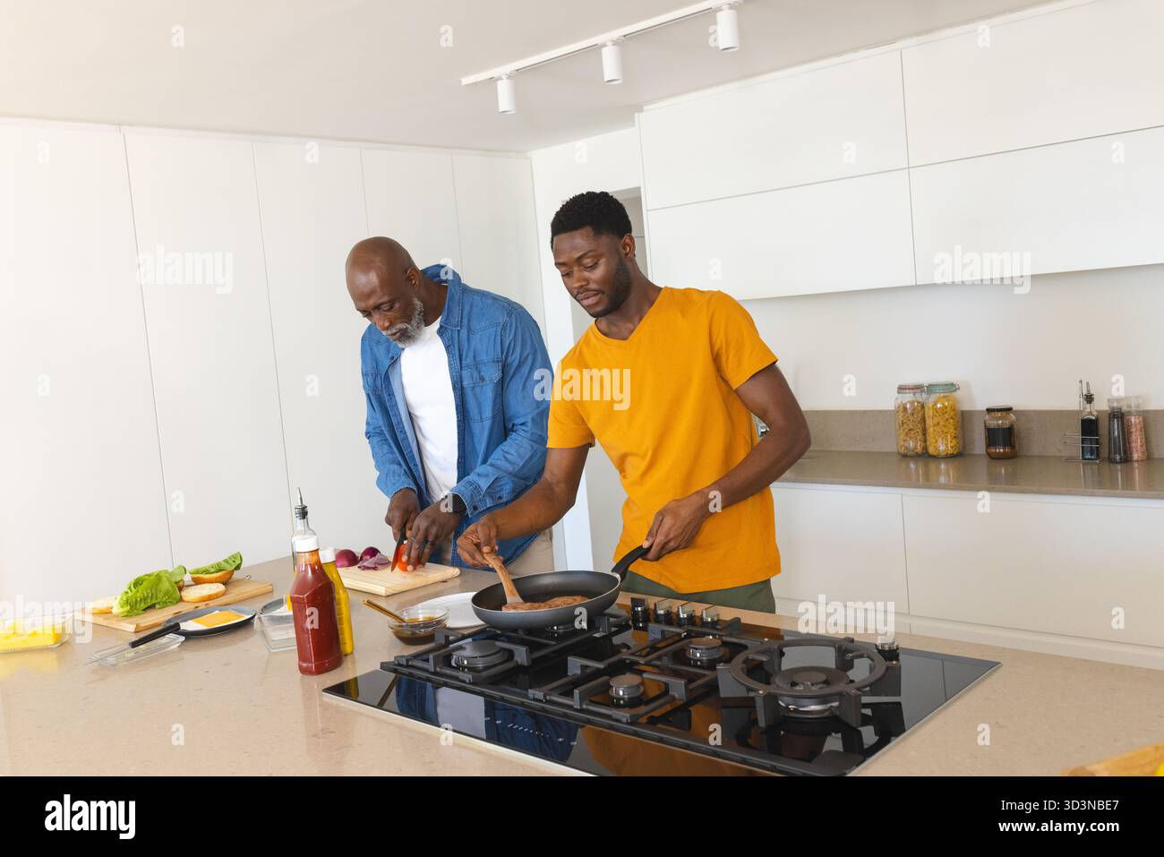 Cucinare padre e figlio afroamericani preparando il pasto in una cucina moderna, con verdure fresche Foto Stock