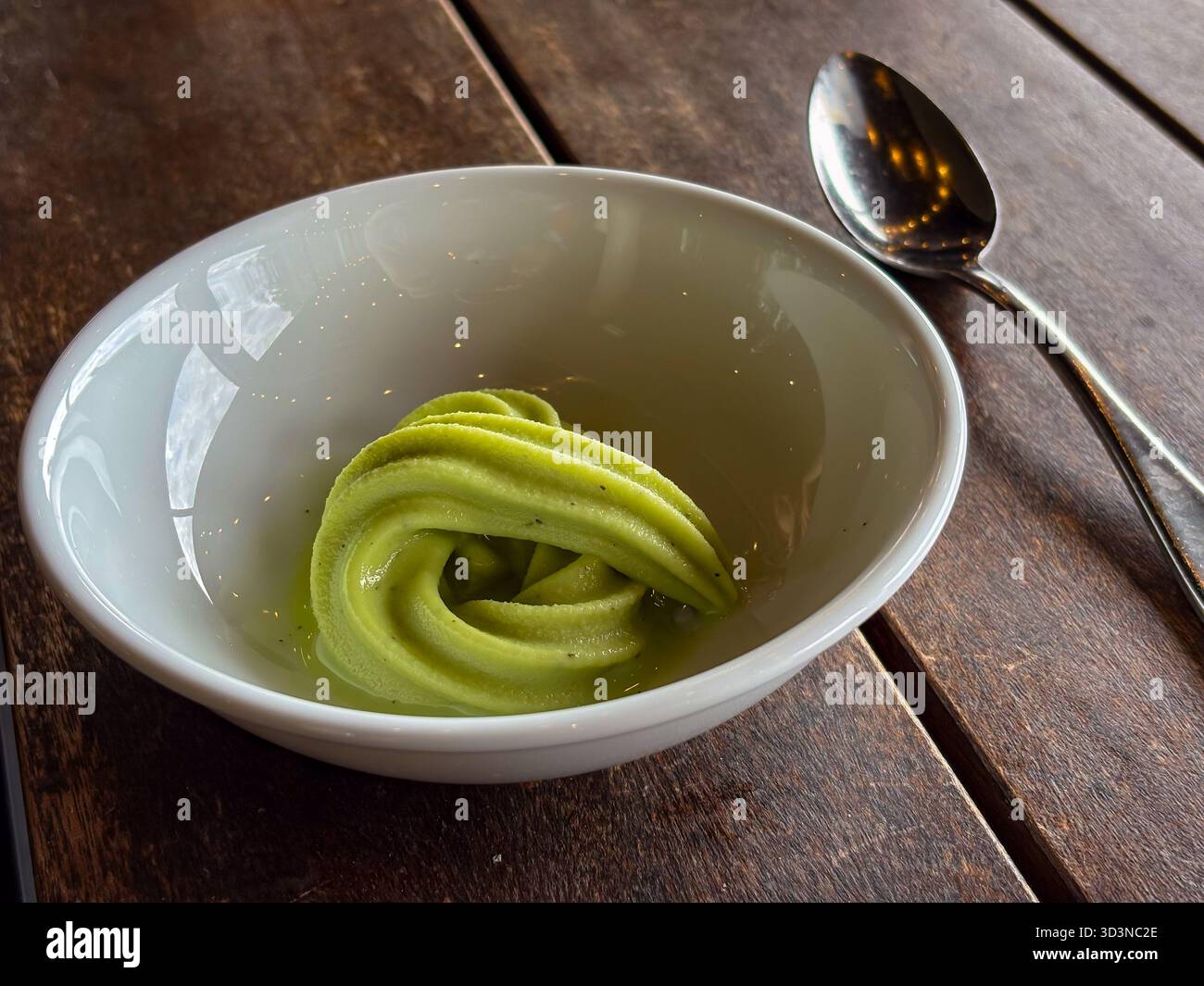 Gelato Kawakawa soffice servito in una ciotola bianca su un rustico tavolo di legno con un cucchiaio, evidenziando il suo colore verde unico e la consistenza cremosa. Foto Stock