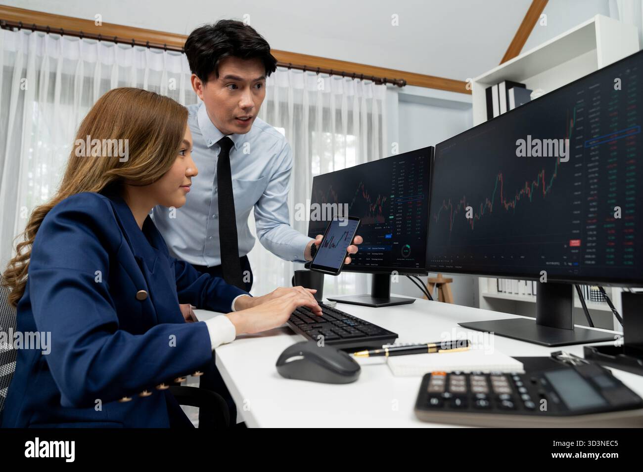 Uomo d'affari asiatico sorridente che mostra dati dinamici del mercato azionario al telefono con una donna che cerca al computer per analizzare il tasso di cambio del valore del profitto Foto Stock