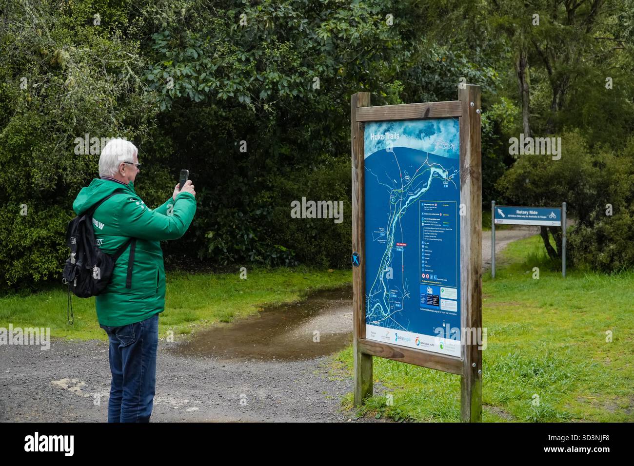 Huka Falls, Taupo, nuova Zelanda. Un turista senior fotografa una mappa dei sentieri con uno smartphone, mostrando attività all'aperto vicino all'iconica cascata. Foto Stock