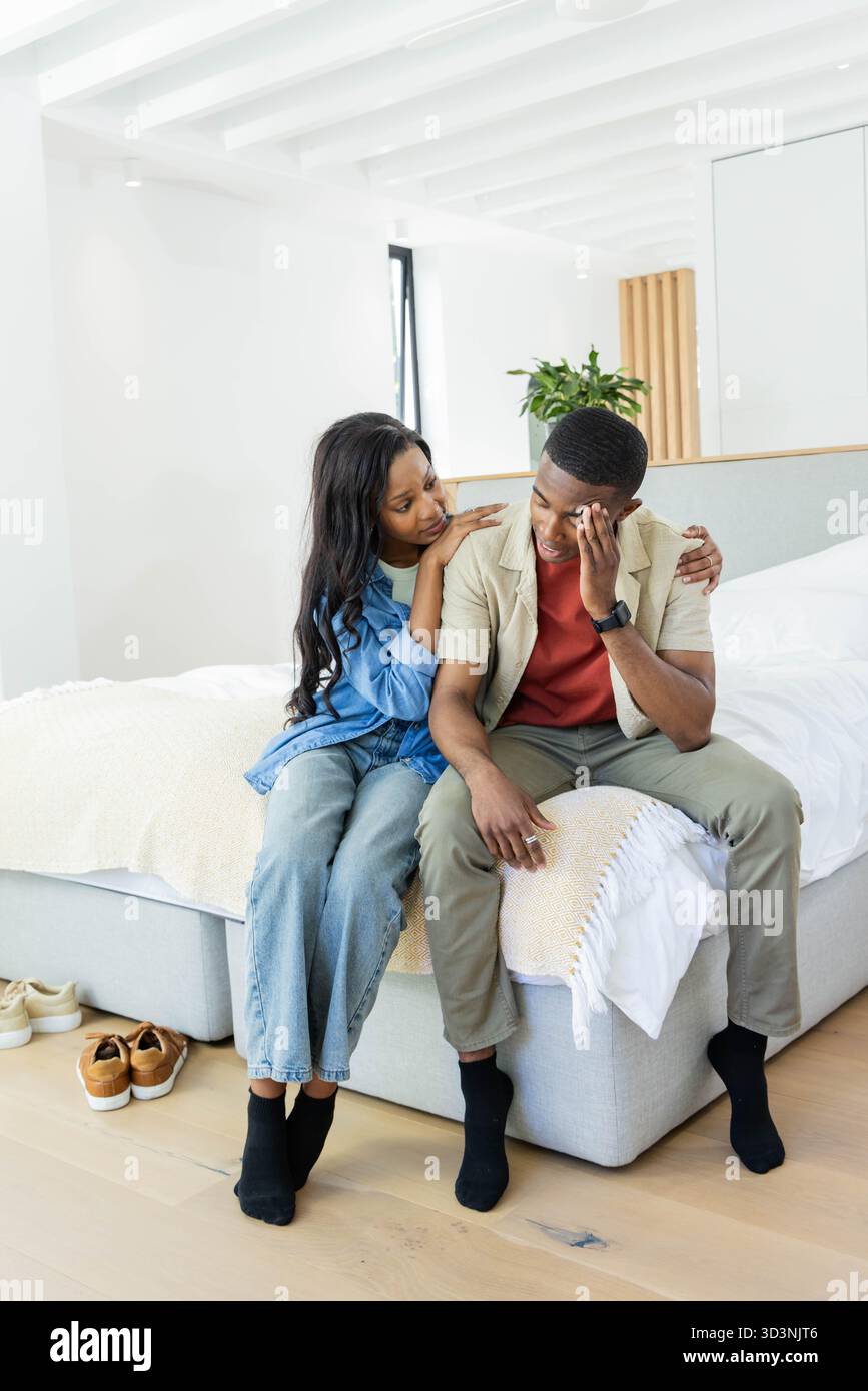 Coppia afroamericana che si confortano e si consolano a vicenda in una camera da letto moderna, con scarpe e piante Foto Stock
