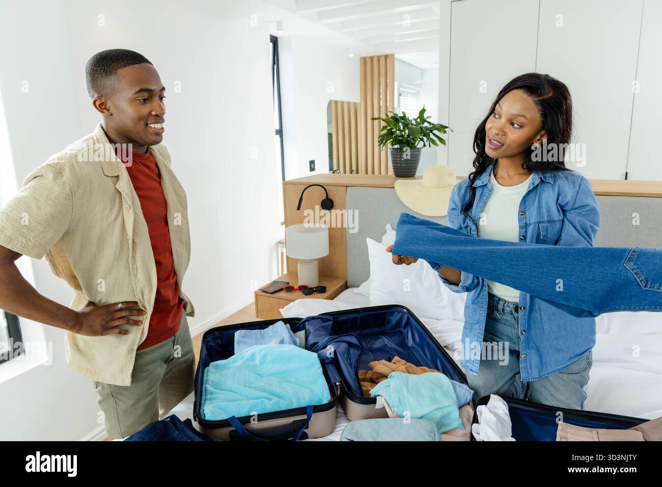 Prepara una coppia afroamericana che prepara una valigia marina aperta in camera da letto, con gli indispensabili per il viaggio Foto Stock